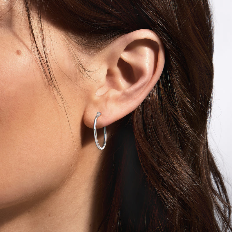 Small hinged white gold hoop earrings on earlobe, close-up