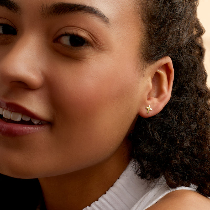 Yellow gold cross stud earring on ear