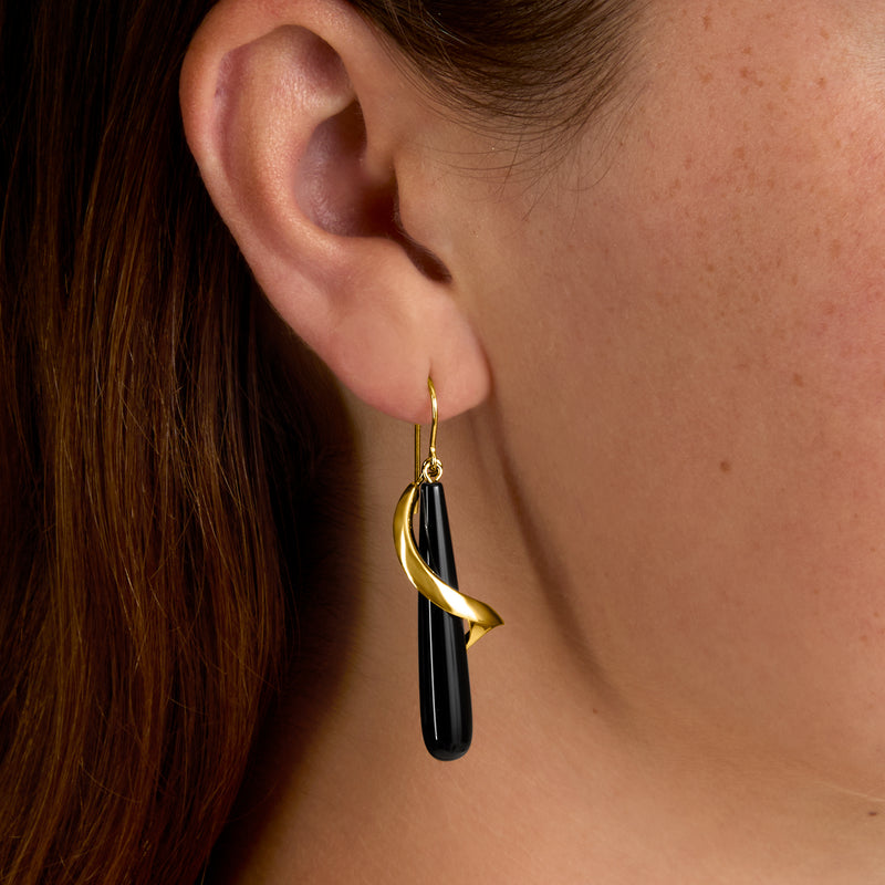 Gold drop earrings with black onyx teardrop and twisted spiral; close-up on ear