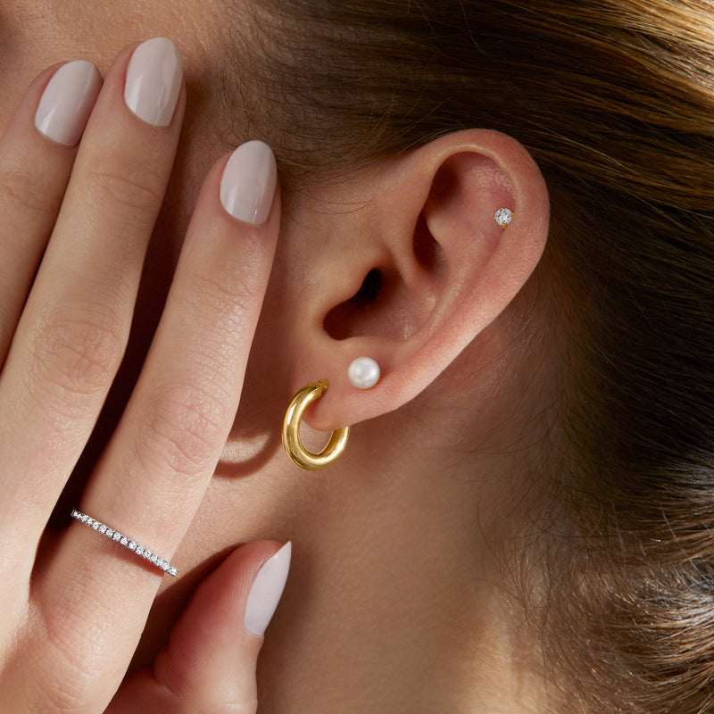 14kt yellow gold huggie hoop earring on ear with small pearl accent