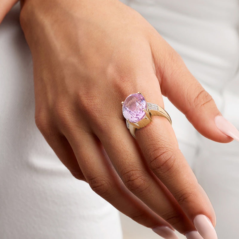 Kunzite and diamond ring on hand with oval pink gemstone in yellow gold band