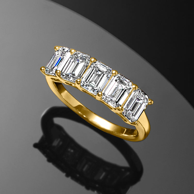 Angled view of five emerald-cut diamonds in yellow gold with round prong accents