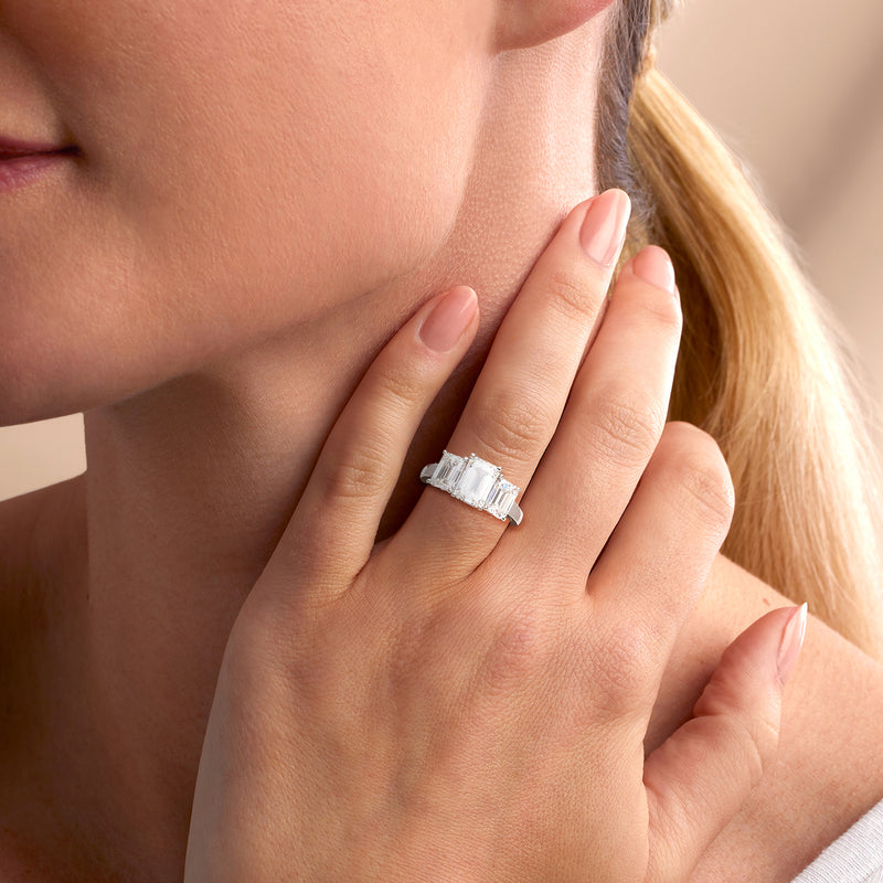 Three-stone emerald-cut diamond ring in 14kt white gold on finger, close-up