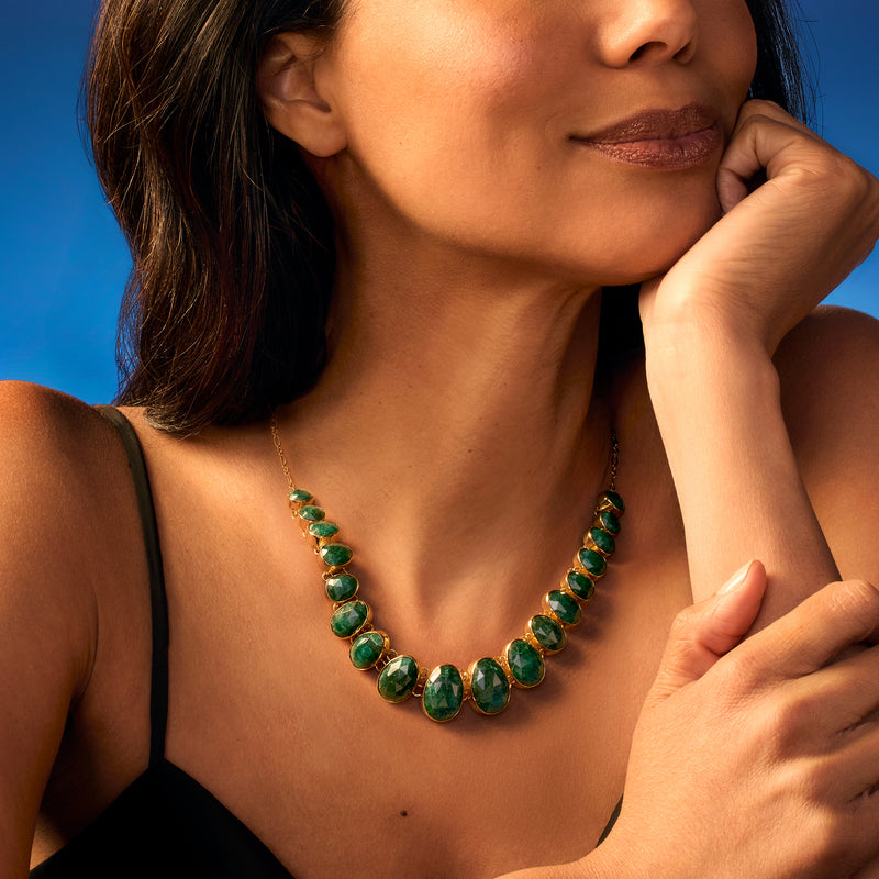 Graduated oval green gemstone necklace on gold chain, worn by woman