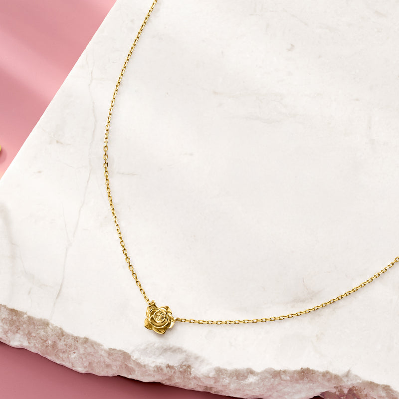 Gold rose pendant necklace on white stone surface