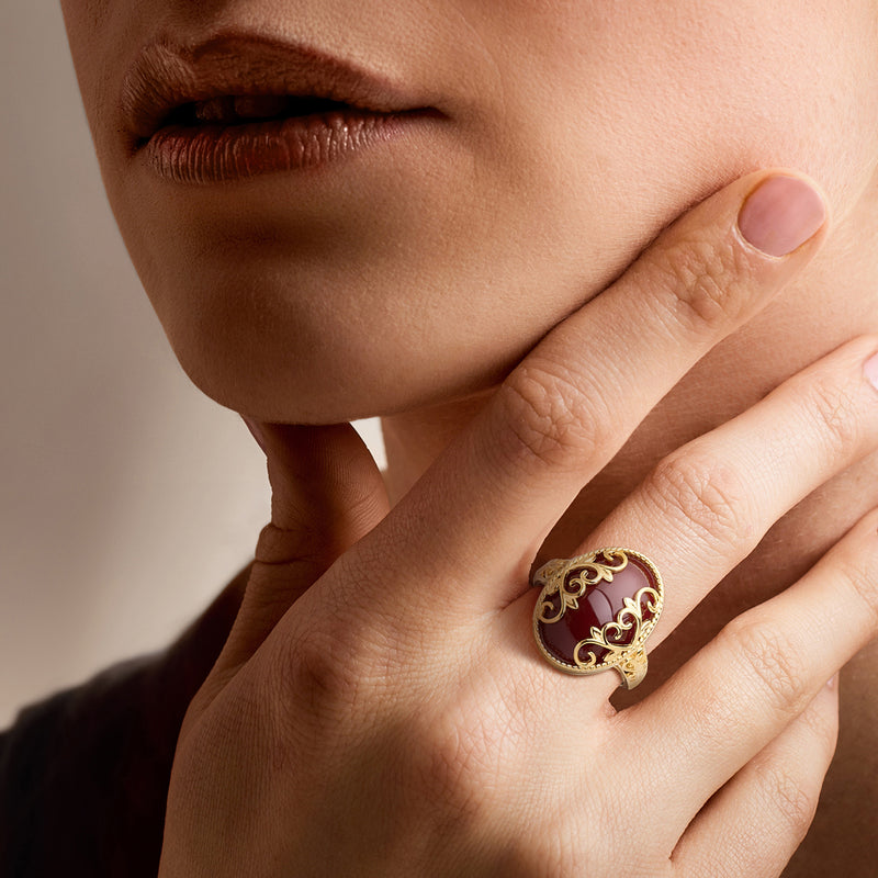 Gold-tone heart-scroll ring with red oval gemstone on finger