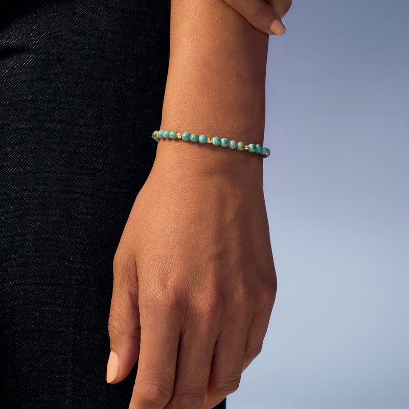Turquoise bead stretch bracelet on wrist with 14kt yellow gold spacer beads