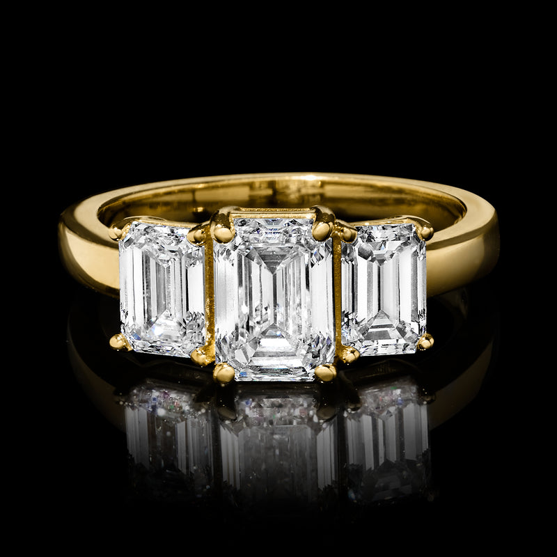 Close-up three-stone emerald-cut diamond ring with yellow gold band and three clear stones