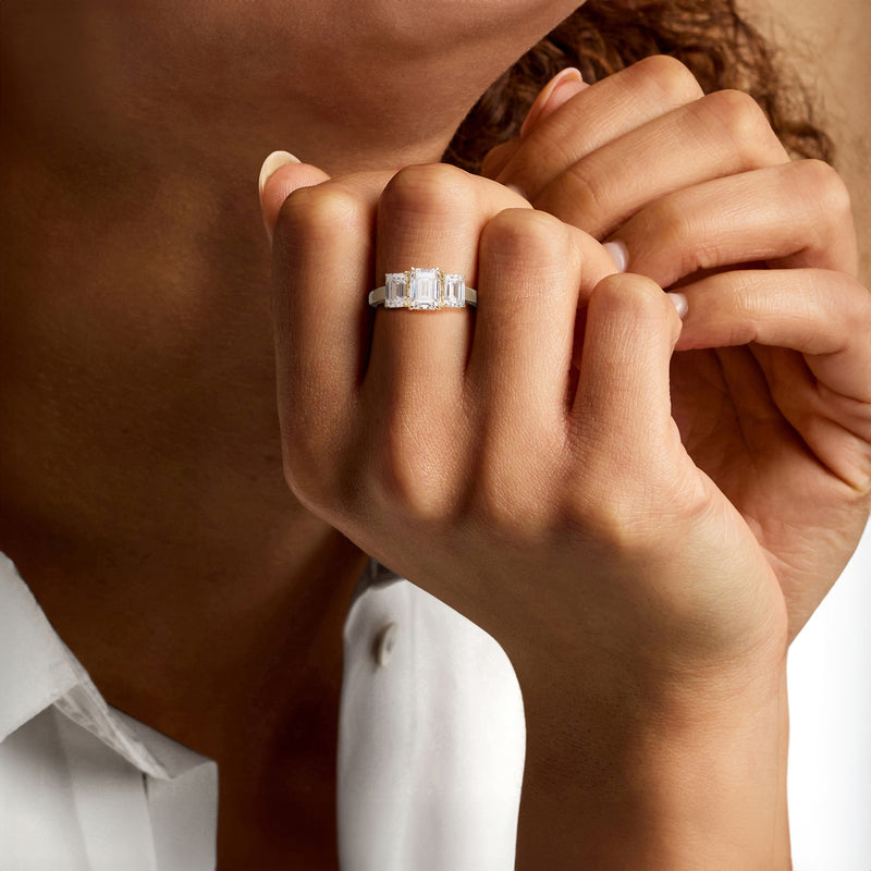 Three-stone emerald-cut diamond ring on hand, yellow gold band with three clear stones