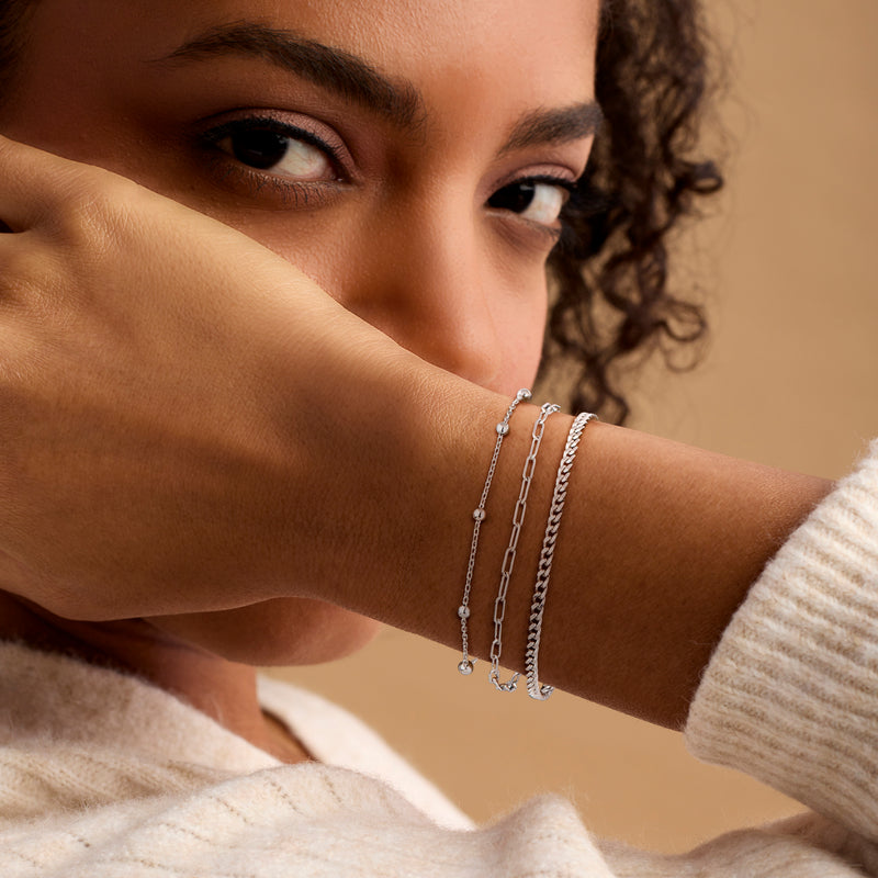 Sterling silver stacked bracelets on wrist: curb-link, paperclip, and bead-chain