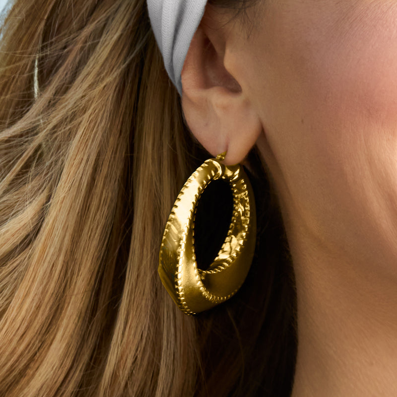 Gold-tone oval hoop earring on wearer’s ear, showing textured outer rim