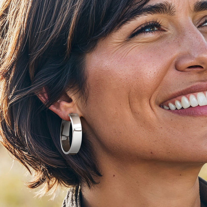 Sterling silver flat hoop earrings on ear, glossy hinged oval hoops