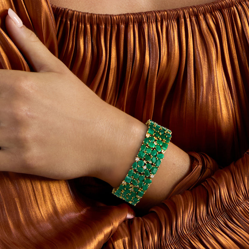 Worn gold bracelet with emerald-green gemstone rows and small white stones on the wrist.