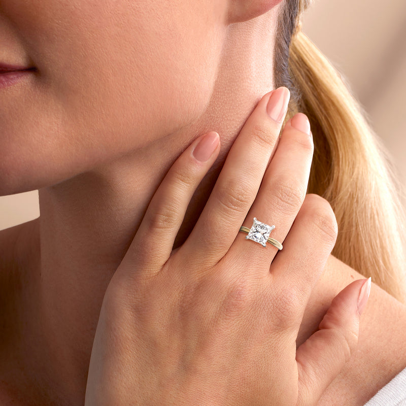 Princess-cut diamond solitaire ring on finger, square center stone in 14kt yellow gold