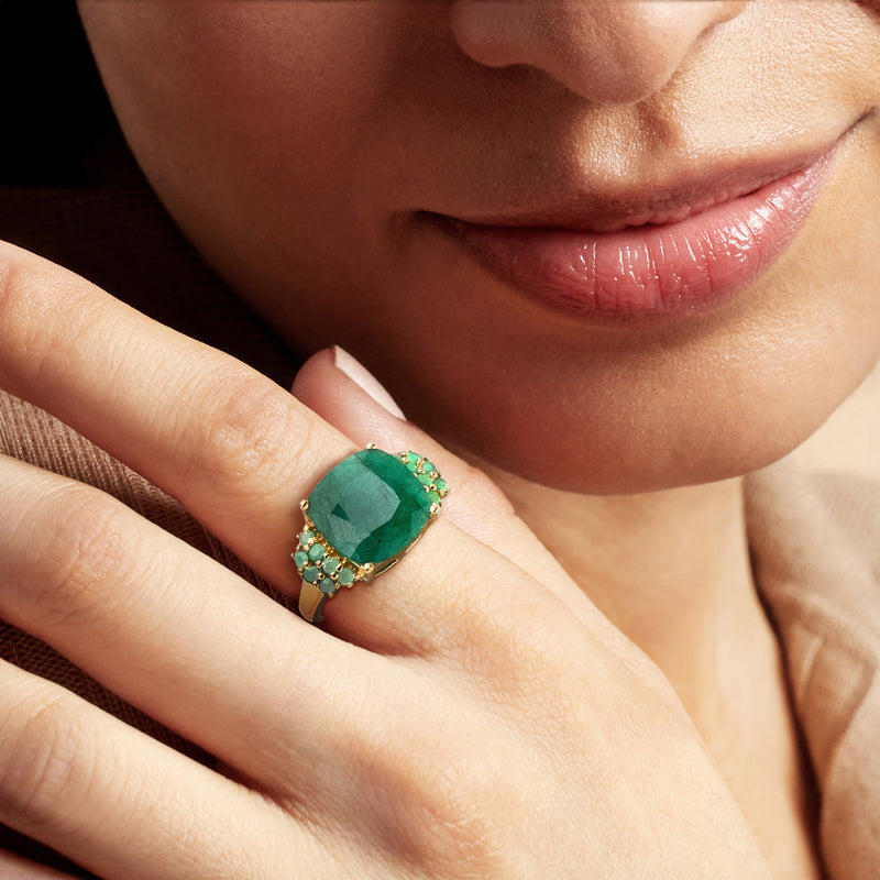 Emerald-green oval gemstone ring on finger, gold setting with green side stones