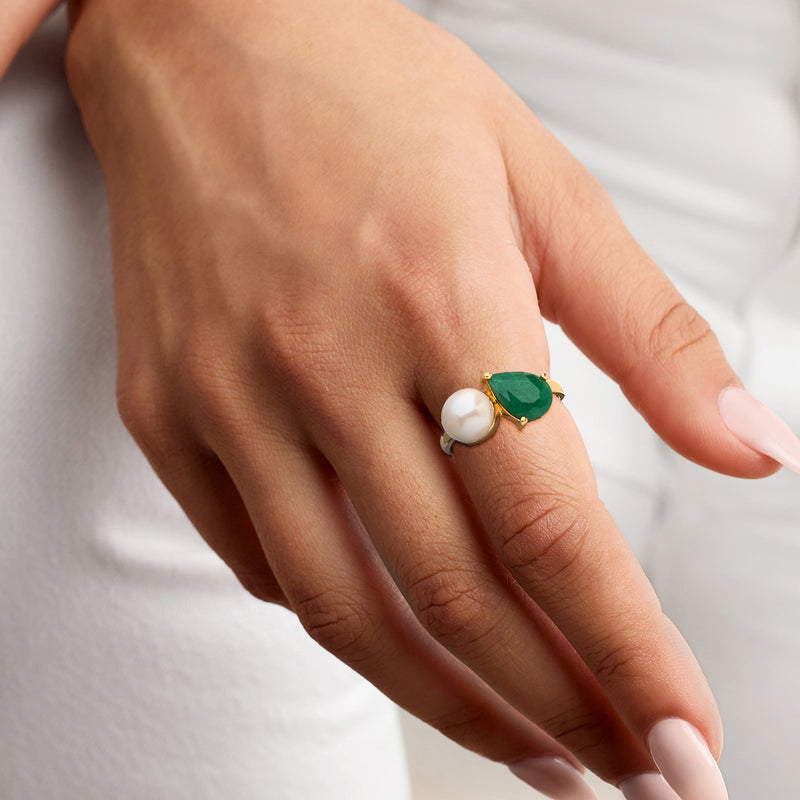 Gold Toi et Moi ring on hand with white pearl and green emerald, slim band and prongs