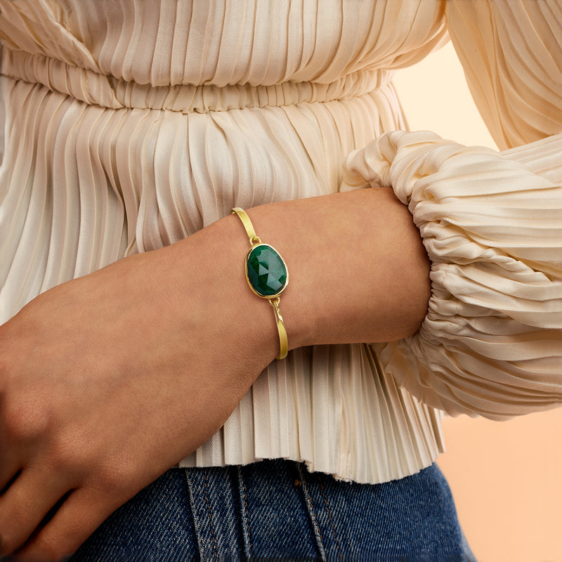 Gold bracelet on wrist with oval green gemstone and hinged bangle setting