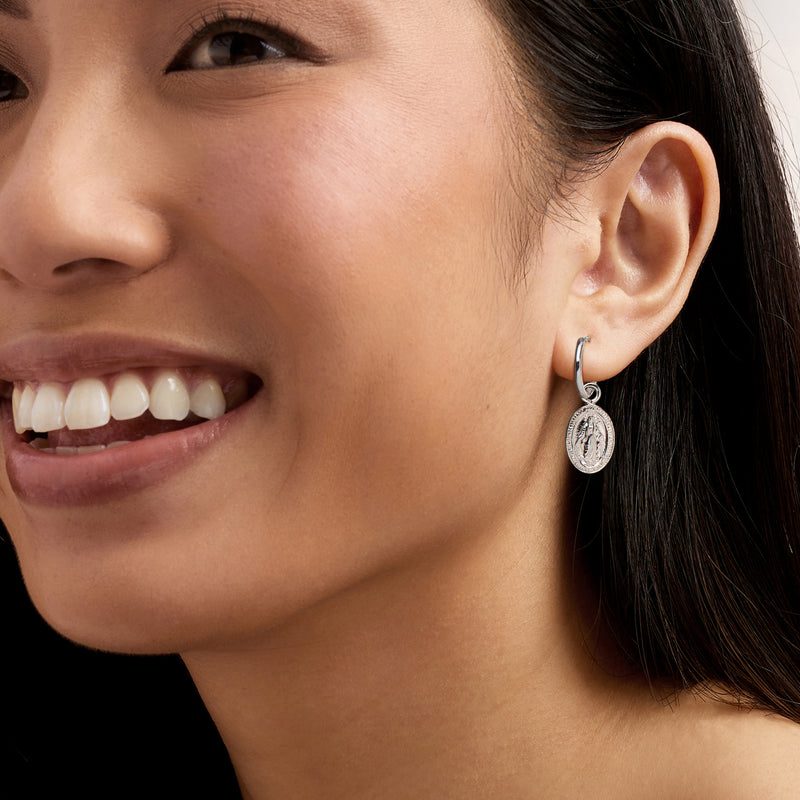 Model wearing sterling silver hoop earring with oval religious medallion drop