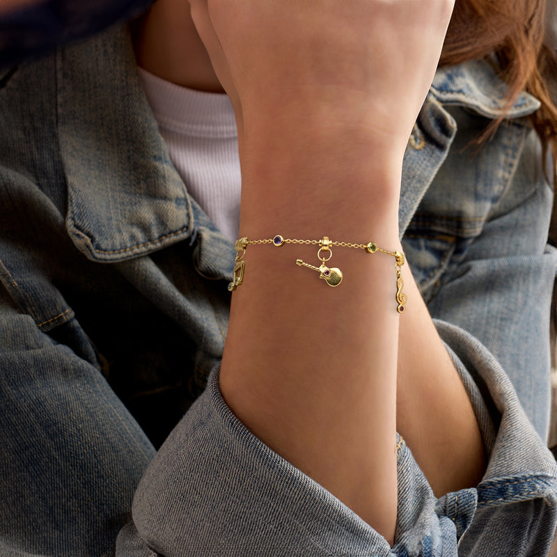Gold-tone musical charm bracelet worn on wrist with small gemstone dangles