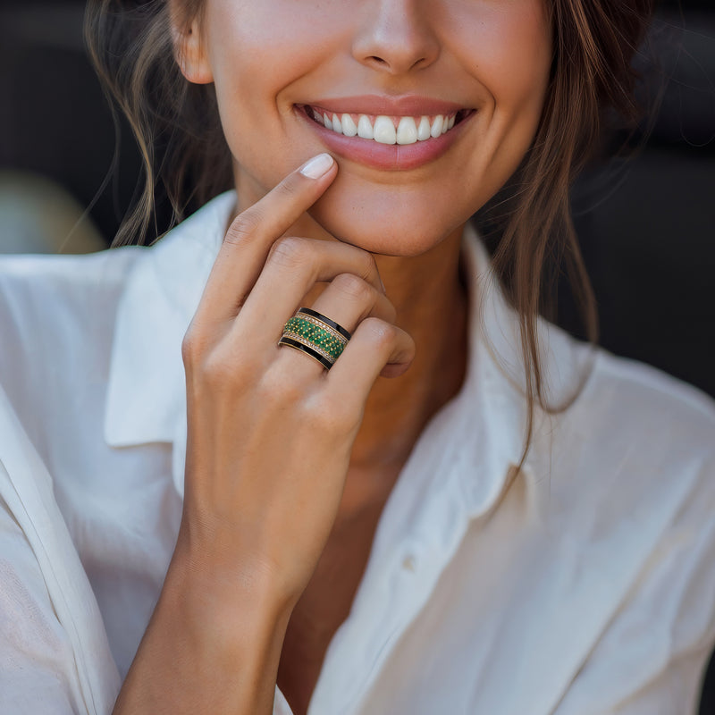 Gold and black enamel ring with green gemstones and white stones on a finger