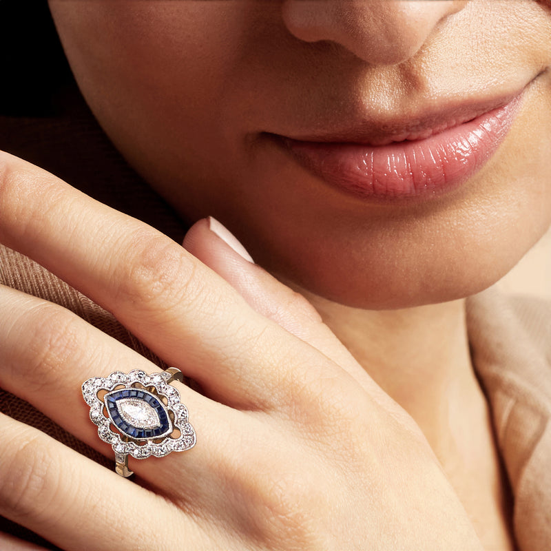 Diamond and blue two-tone gold ring worn on finger, oval blue center and halo