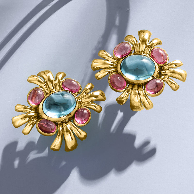 Close-up gold clip-on earrings: oval blue center surrounded by pink round stones.
