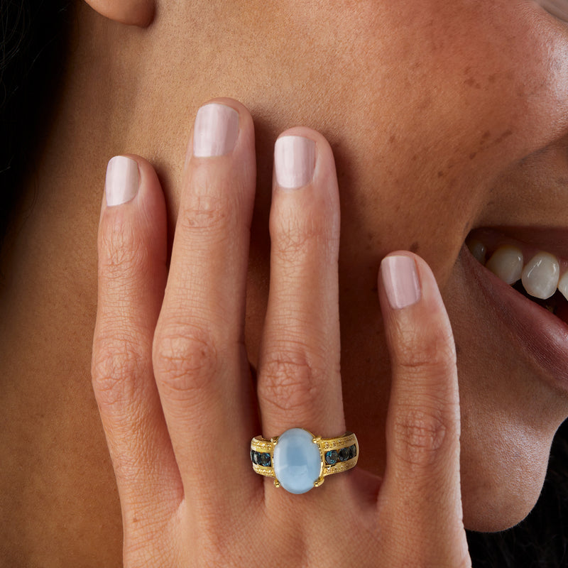 Gold-tone ring on finger with oval light-blue stone and blue gemstone accents