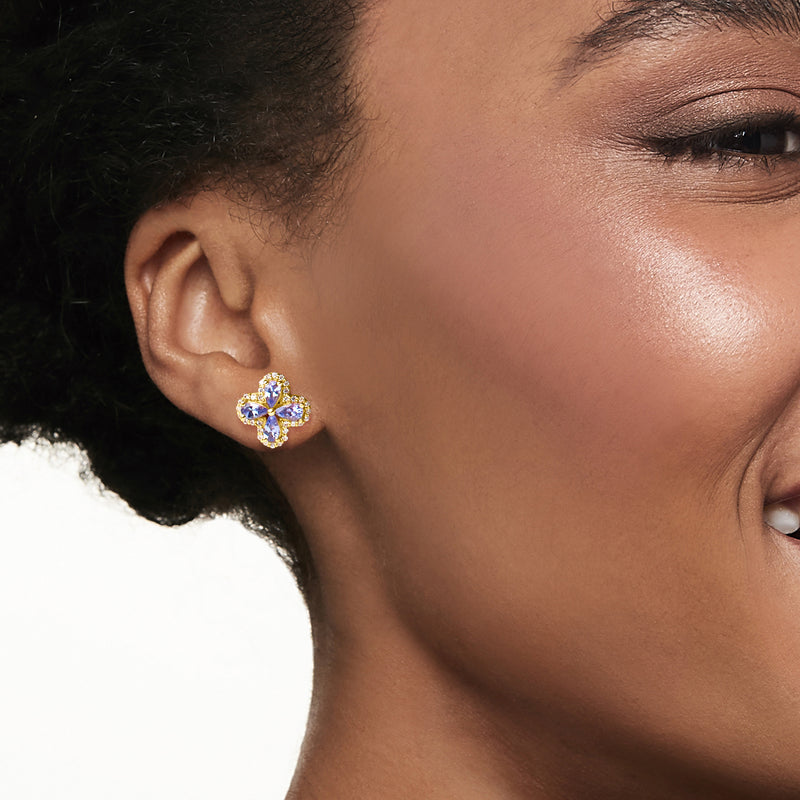 Floral post earrings on ear, blue oval tanzanite stones with white zircon in gold over sterling