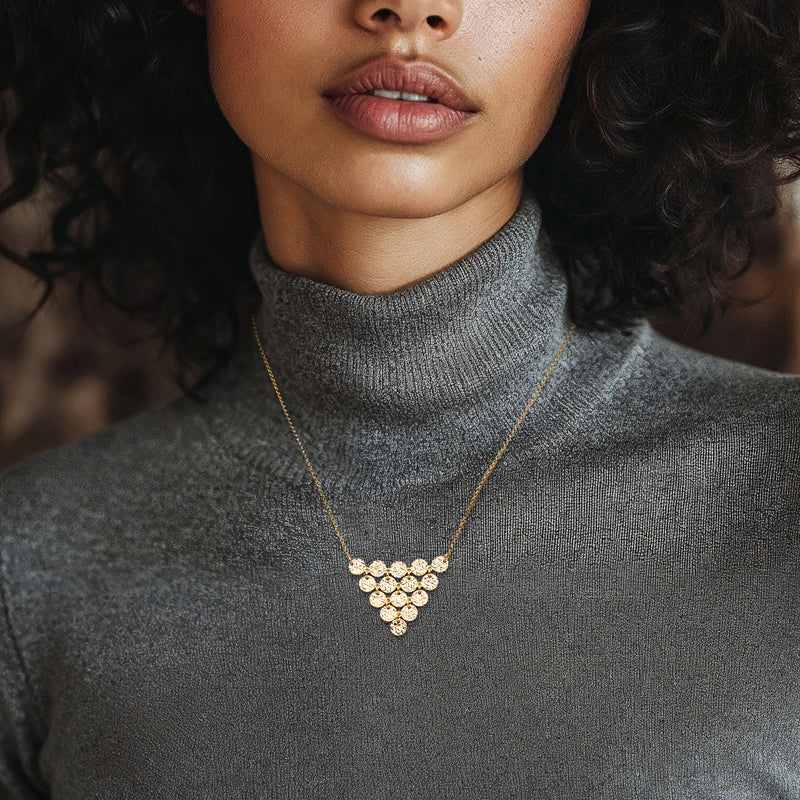 Gold multi-disc heart drop necklace on fine chain, worn with high neckline