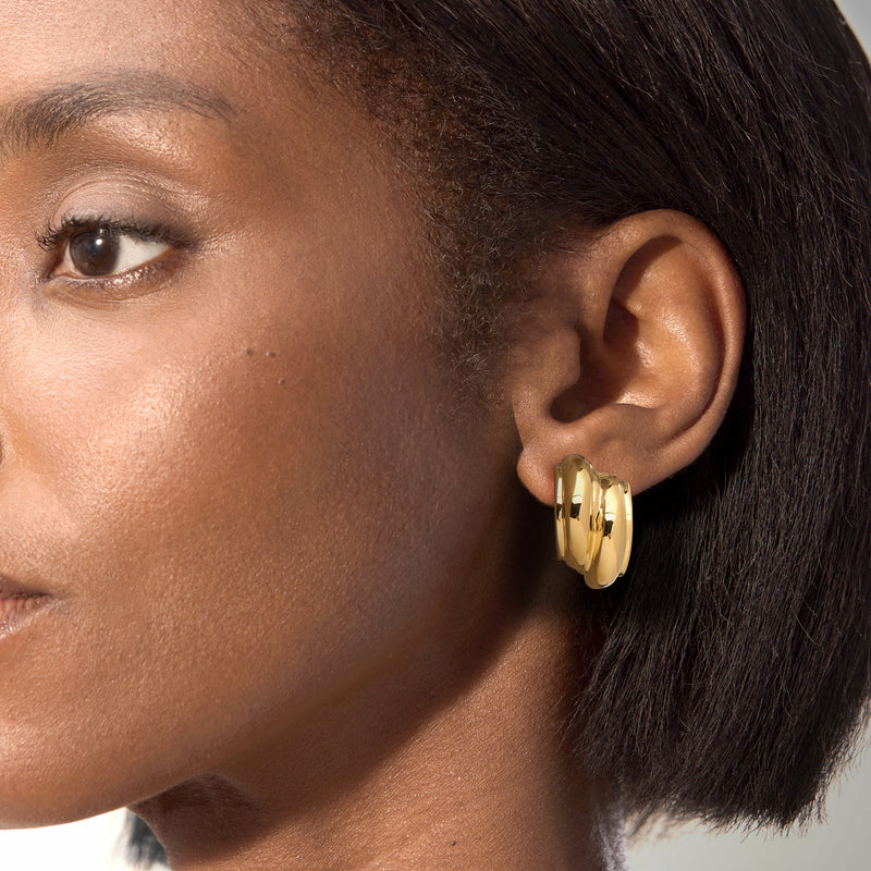 Curved ribbed gold-tone post earrings on model ear, close-up view