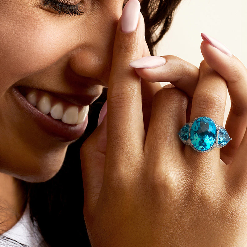 Swiss blue topaz ring on finger, oval blue stone with white gold setting and diamond trim