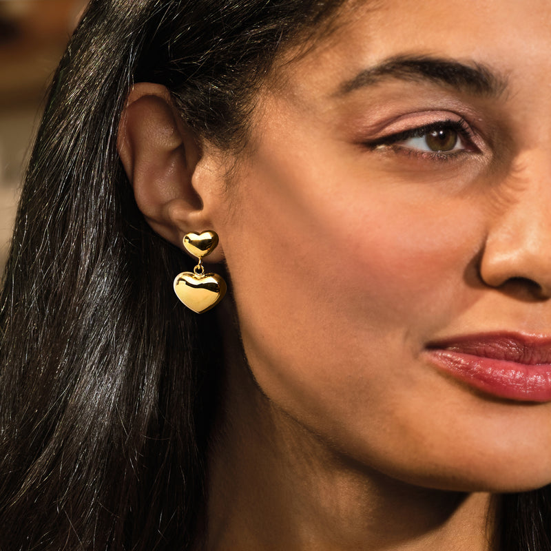 Gold heart drop earrings with double puffed hearts, worn on ear