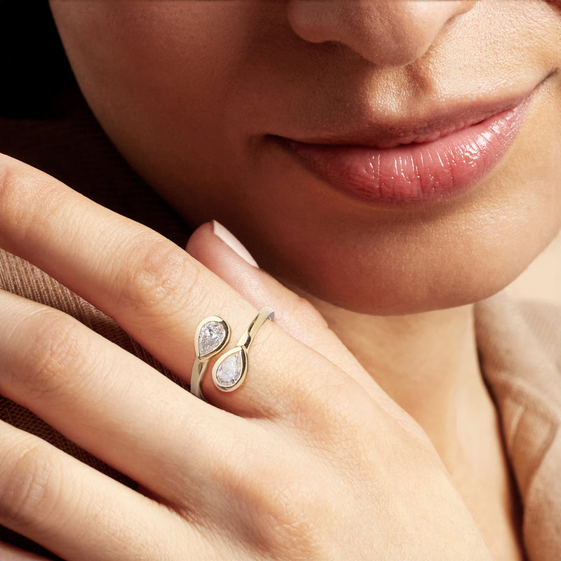 Yellow gold bypass ring with two oval lab-grown diamonds on finger, close-up