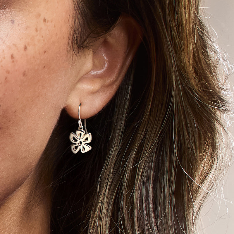 Sterling silver flower drop earrings on ear, small four-petal hoop-hang style