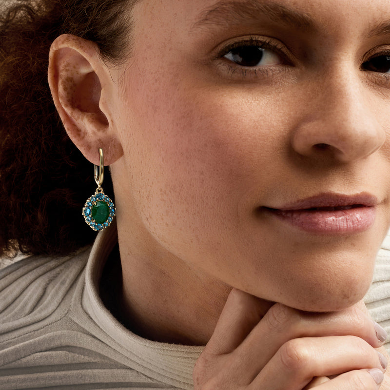 Gold drop earrings on model: oval green center with blue halo gemstones.