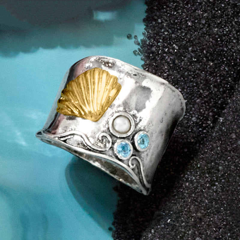 Angled seashell ring featuring gold shell, white pearl, and blue gemstone clusters in silver