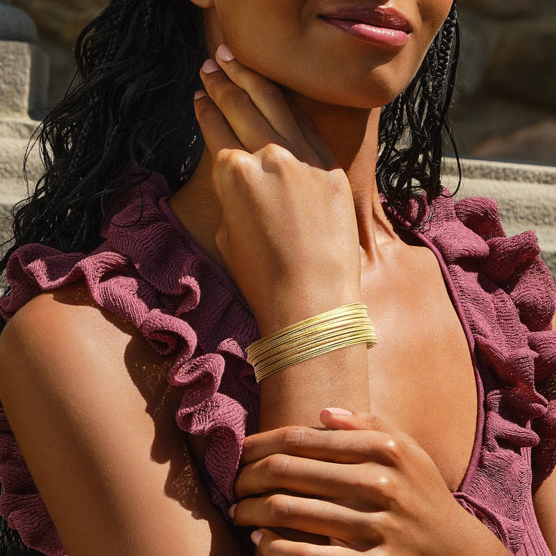 Gold multi-row bangle bracelet worn on wrist, stacked bands with textured finish