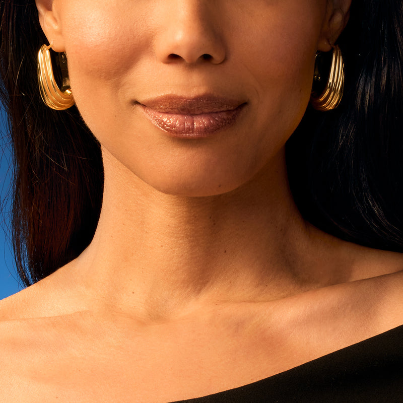 Yellow gold ribbed hoop earrings, oval hoops framing the ear, polished shine