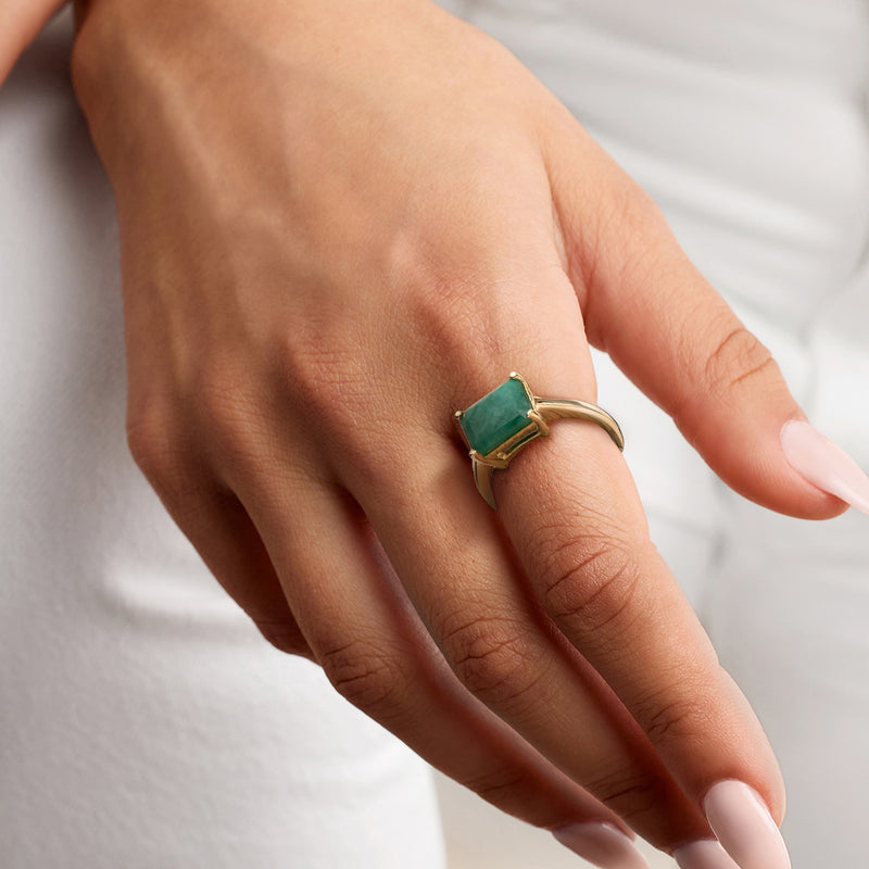 Gold ring with emerald-green square gemstone worn on a hand