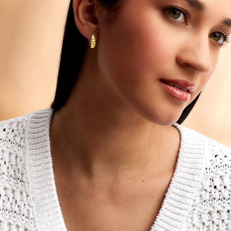 Ribbed yellow gold huggie hoop earrings worn on the ear