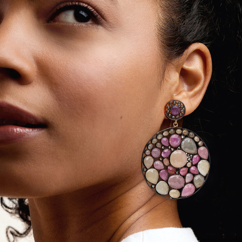 Gold-tone round disc drop earrings with multicolored gemstones, worn close-up on ear