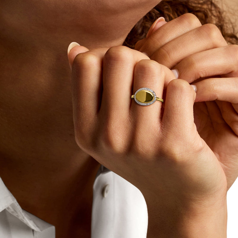 Yellow gold oval monogram ring with diamond halo worn on finger