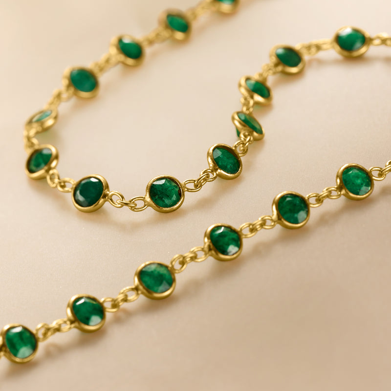 Close-up of gold chain with bezel-set green emeralds in round settings