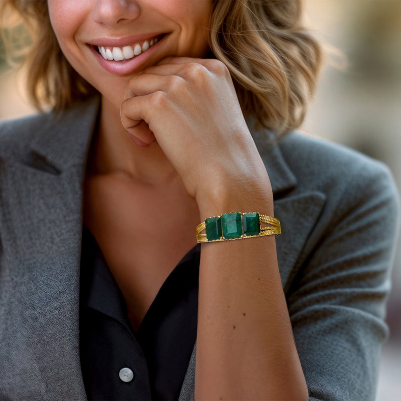 Gold-tone cuff bracelet on wrist with three emerald green rectangular stones