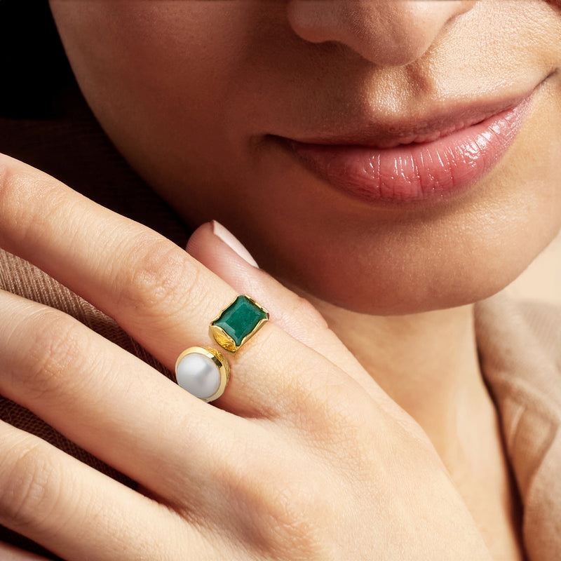 Gold ring close-up on finger: white pearl and green emerald with golden band