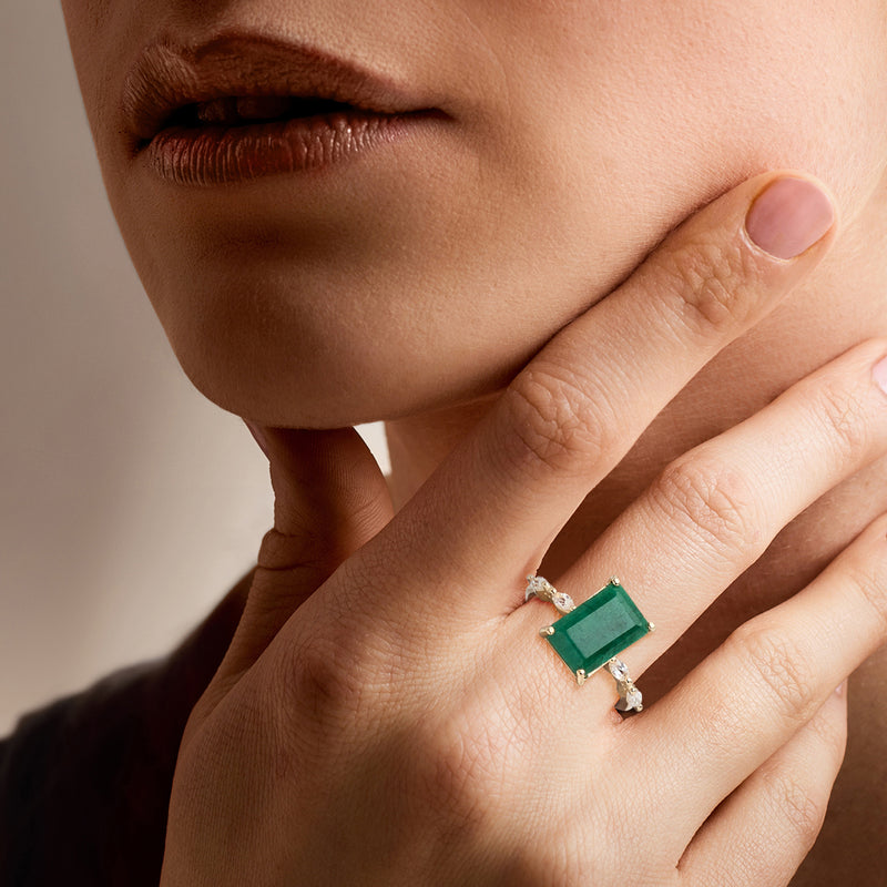 Hand wearing gold ring with emerald-cut green stone and white topaz detail