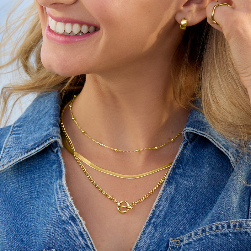 Layered gold curb-link toggle necklaces, each with loop clasp and small links