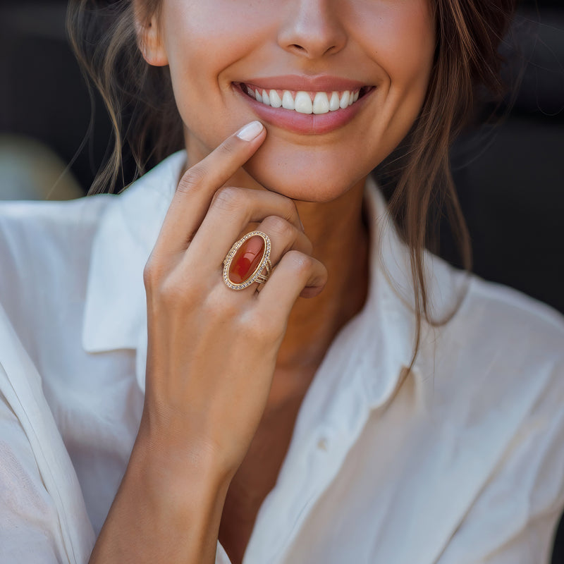 Gold gemstone ring worn on finger, oval orange stone with diamond-like halo