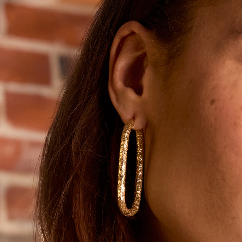 Hammered gold hoop earring with rectangular silhouette, side view on ear