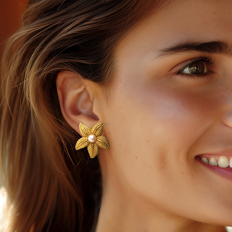 Woman wearing yellow gold starfish earrings with textured petals and white pearl